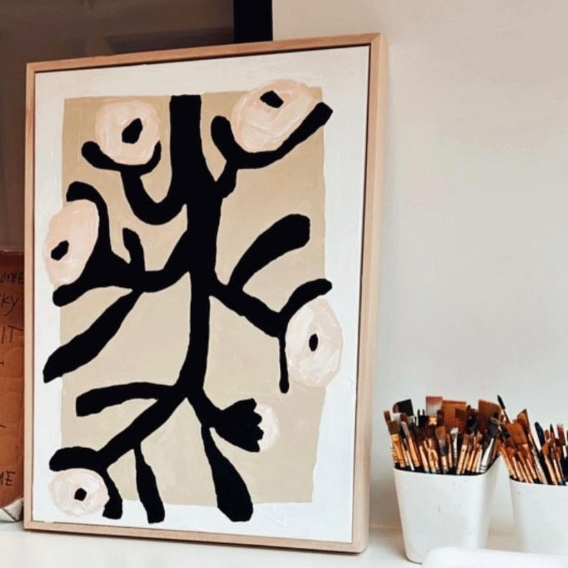 Black and white abstract painting of flowers in frame sitting next to jars of paintbrushes.