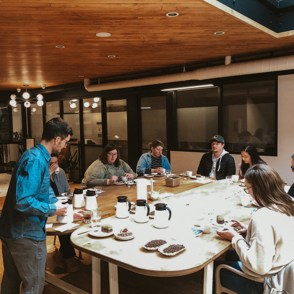 A group of coffee lovers sitting at a table being led in a coffee tasting by our roaster.